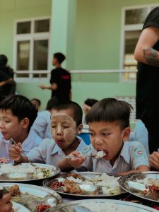 Group of children eating lunch together outside at school, sharing a joyful meal.