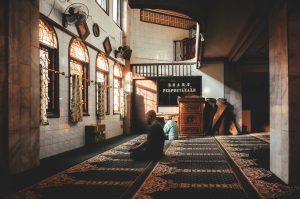 Tranquil scene of two men in peaceful reflection within a sunlit mosque interior, showcasing cultural architecture.