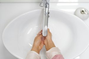 A woman washing her hands under a chrome faucet in a white sink, emphasizing hygiene.